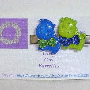 May include: Two colorful barrettes with a green and blue zebra design. The barrettes are attached to a silver metal clip. The text "Girly Girl Barrettes" is printed on the white background. Etsy store: https://www.etsy.com/shop/SarahsVarietyShoppe