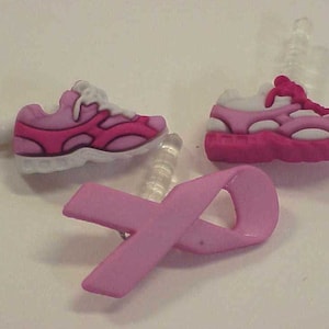 May include: Three pink and white shoe charms with a pink ribbon charm. The shoe charms are designed to look like running shoes. The ribbon charm is a symbol of breast cancer awareness.