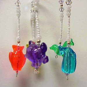 May include: Four colorful glass animal figurines hanging from white beaded strings. The figurines are a red fish, a purple turtle, a green dolphin, and a blue seahorse.