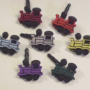 May include: Set of six colorful plastic toy train phone charms. The trains are red, blue, gray, yellow, purple, and green. Each train has a black plastic base and a black plastic antenna.