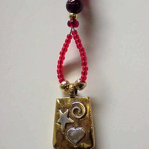May include: A gold pendant with a heart, star, and swirl design hangs from a red beaded necklace.