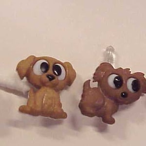 May include: Four brown dog-themed phone charms with clear plastic loops. The charms include a paw print, a brown dog with pink ears, a brown dog with brown ears, and a brown dog with brown ears and a white spot on its chest.