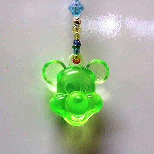 May include: A green plastic charm of a cartoon mouse head with large ears. The charm is attached to a beaded string.