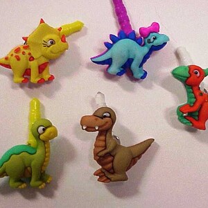 May include: Five colorful dinosaur-shaped phone charms. The charms are made of plastic and have a variety of colors, including green, yellow, blue, orange, and red. The charms are designed to be attached to a phone case or other accessories.