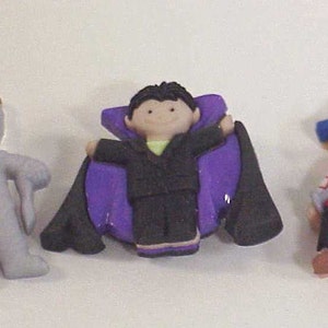 May include: Three Halloween costume buttons featuring a gray monster, a vampire with a purple cape, and a pirate with a blue hat and eyepatch.