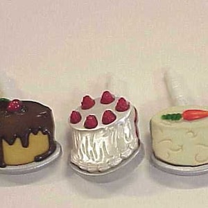 May include: Five miniature cake toppers, each with a different design and color. The toppers are made of plastic and have a small metal stand on the bottom. The cakes are decorated with frosting, sprinkles, and fruit.