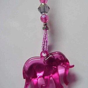 May include: A pink plastic elephant charm hangs from a pink and silver beaded chain. The elephant charm has a detailed design and is a cute and whimsical accessory.