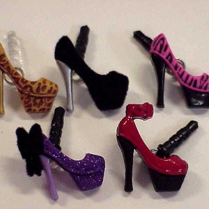 May include: Five different high heel shoe charms in various colors and patterns. The charms are made of plastic and have a metal loop for attaching to a phone case or other accessories.