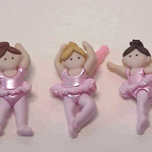 May include: Three pink ballerina figurines with brown, blonde, and brown hair. Each figurine is wearing a pink tutu and pink shoes.