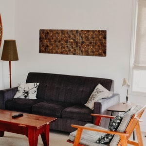 Op de afbeelding: Een woonkamer met een donkergrijze bank, een houten salontafel, een houten fauteuil en een houten vloer. Er hangen twee sneeuwschoenen aan de muur, een lamp met een bruine lampenkap en een rechthoekig wandkunstwerk boven de bank.