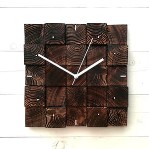 Puede incluir: Un reloj de pared cuadrado hecho de bloques de madera marrón oscuro con manecillas blancas. La esfera del reloj está hecha de una cuadrícula de bloques de madera.