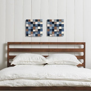 May include: A wooden bed frame with a white headboard and white bedding. Two small square abstract art pieces hang on the wall behind the bed.