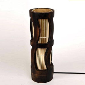 Peut inclure: Une lampe en bambou brun foncé avec un motif tissé. La lampe a une forme cylindrique et une finition naturelle.