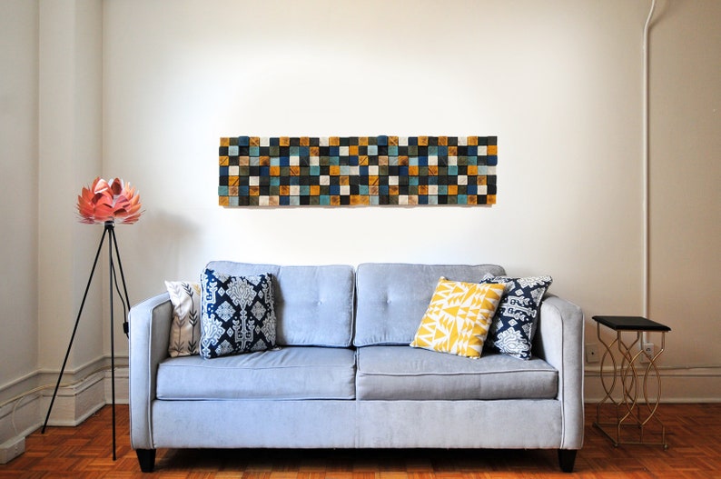 Puede incluir: Un sof&aacute; gris con tres almohadas, una amarilla, una azul y blanca con estampado y una azul con estampado. Una l&aacute;mpara de flores rosa est&aacute; a la izquierda del sof&aacute;. Un arte de pared geom&eacute;trico en blanco y negro est&aacute; sobre el sof&aacute;.