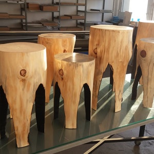 May include: Six wooden stools with natural wood grain and black painted legs. The stools are arranged in a row on a glass table.