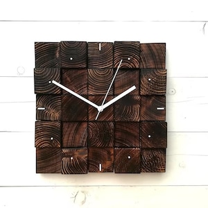Puede incluir: Un reloj de pared cuadrado hecho de bloques de madera marr&oacute;n oscuro con manecillas blancas. La esfera del reloj est&aacute; hecha de una cuadr&iacute;cula de bloques de madera.