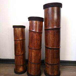 May include: Three brown bamboo vases of varying heights with dark brown rope trim around the top and bottom.