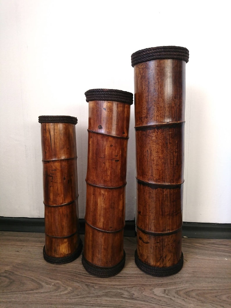 May include: Three brown bamboo vases of varying heights with dark brown rope trim around the top and bottom.