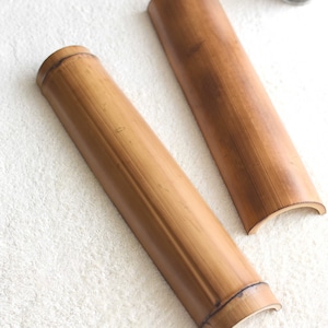 May include: Two brown bamboo rollers, each with a rounded end, are lying on a white fluffy surface. The rollers are made of natural bamboo and have a smooth, polished finish.