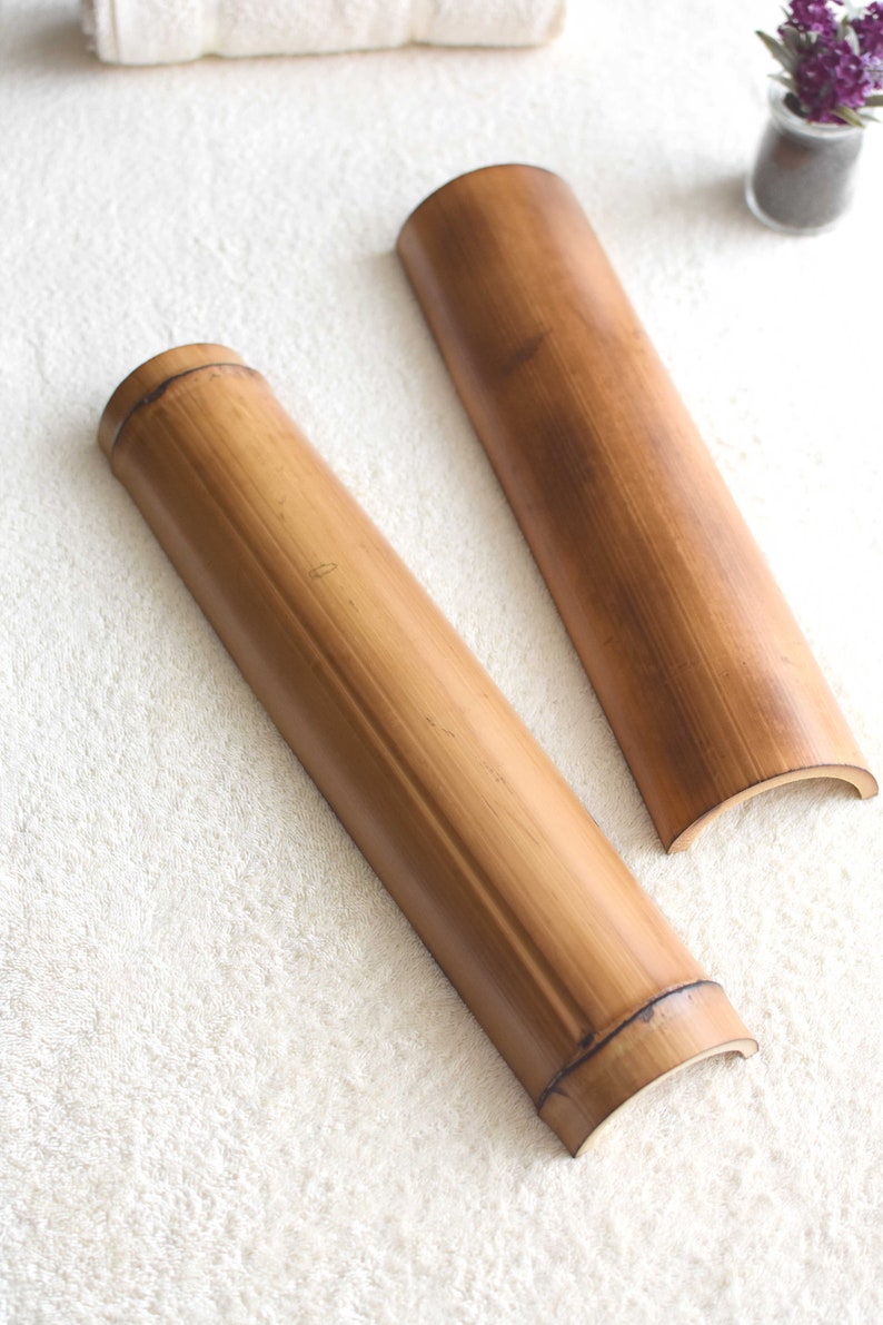 May include: Two brown bamboo rollers, each with a rounded end, are lying on a white fluffy surface. The rollers are made of natural bamboo and have a smooth, polished finish.