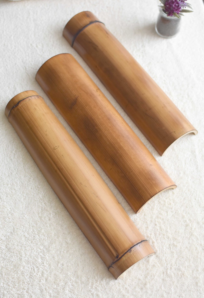 May include: Three natural brown bamboo rollers of varying sizes. The rollers are curved on one end and flat on the other. The rollers are arranged in a row on a white fluffy surface.