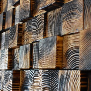 Puede incluir: Una pared hecha de peque&ntilde;os bloques de madera cuadrados. Los bloques est&aacute;n dispuestos en un patr&oacute;n escalonado y tienen un color marr&oacute;n oscuro, casi negro, con veta de madera visible. Los bloques est&aacute;n dispuestos de manera que crean una superficie texturizada y visualmente interesante.