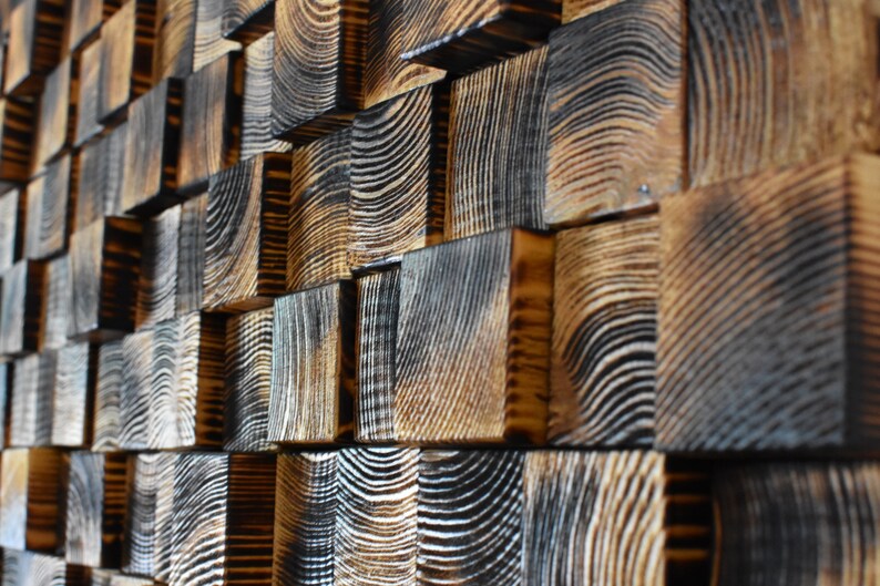 Puede incluir: Una pared hecha de peque&ntilde;os bloques de madera cuadrados. Los bloques est&aacute;n dispuestos en un patr&oacute;n escalonado y tienen un color marr&oacute;n oscuro, casi negro, con veta de madera visible. Los bloques est&aacute;n dispuestos de manera que crean una superficie texturizada y visualmente interesante.