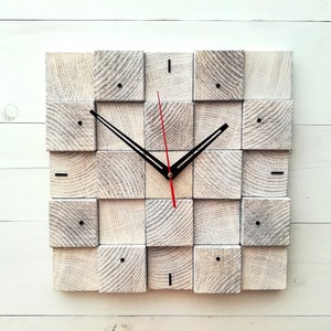 Puede incluir: Un reloj de madera blanco con agujas negras y una aguja de segundos roja. La esfera del reloj est&aacute; formada por 16 cuadrados peque&ntilde;os.