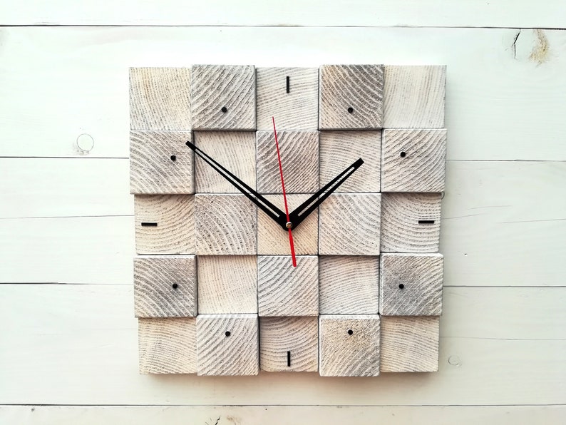 Puede incluir: Un reloj de madera blanco con agujas negras y una aguja de segundos roja. La esfera del reloj est&aacute; formada por 16 cuadrados peque&ntilde;os.