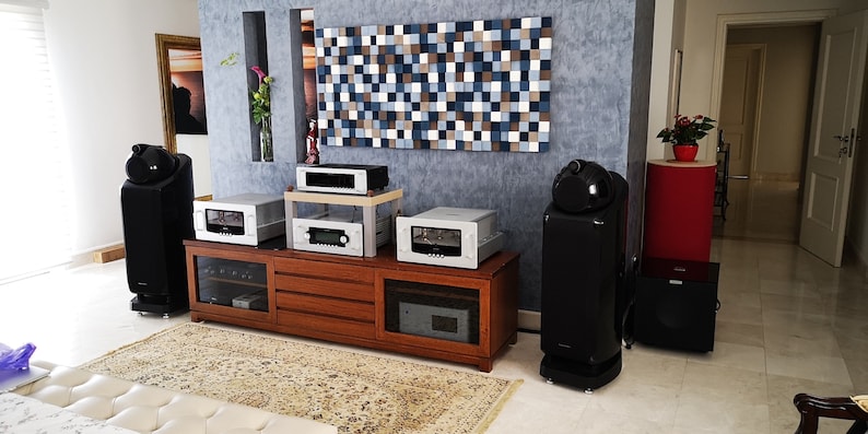 May include: A home audio system with two large black speakers, a wooden entertainment center with multiple audio components, and a subwoofer. The speakers have a unique design with a rounded top and a black finish. The entertainment center has a wood grain finish and multiple drawers. The subwoofer is black and has a rounded shape.