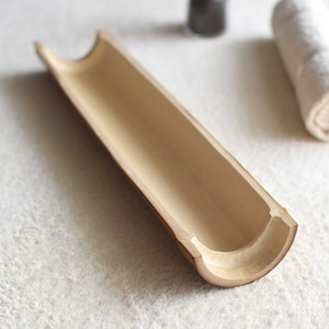 May include: A natural bamboo tray with a smooth, light brown finish. The tray is hollowed out and has a curved shape, making it ideal for holding small items.