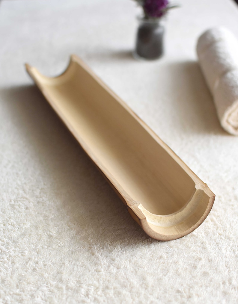 May include: A natural bamboo tray with a smooth, light brown finish. The tray is hollowed out and has a curved shape, making it ideal for holding small items.