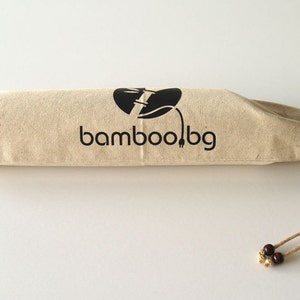 May include: A beige drawstring bag with a black logo that says "bamboo!bg" and a black graphic of a bamboo stalk with a plug on the end. The bag has brown wooden beads on the drawstring.