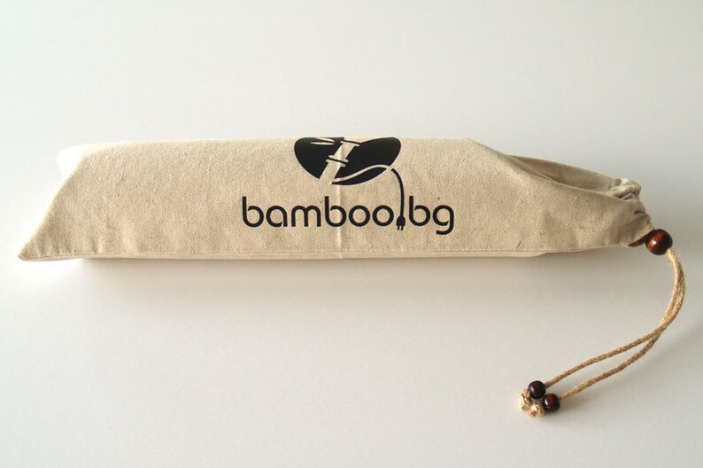 May include: A beige drawstring bag with a black logo that says "bamboo!bg" and a black graphic of a bamboo stalk with a plug on the end. The bag has brown wooden beads on the drawstring.