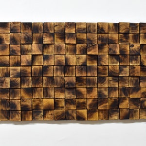 Puede incluir: Una pieza de arte de pared hecha de peque&ntilde;os bloques de madera cuadrados. Los bloques est&aacute;n dispuestos en un patr&oacute;n aleatorio y tienen un acabado de madera oscura quemada.