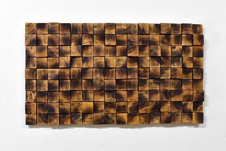 Puede incluir: Una pieza de arte de pared hecha de peque&ntilde;os bloques de madera cuadrados. Los bloques est&aacute;n dispuestos en un patr&oacute;n aleatorio y tienen un acabado de madera oscura quemada.