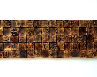 Puede incluir: Una pieza de arte de pared hecha de bloques de madera marrón oscuro dispuestos en un patrón escalonado. Los bloques tienen una veta de madera natural y son ligeramente texturizados.