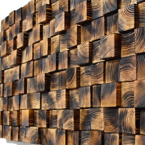 Puede incluir: Una pieza de arte de pared hecha de cuadrados de madera quemada, dispuestos en un patr&oacute;n escalonado. La madera tiene un color marr&oacute;n oscuro con patrones de veta visibles.