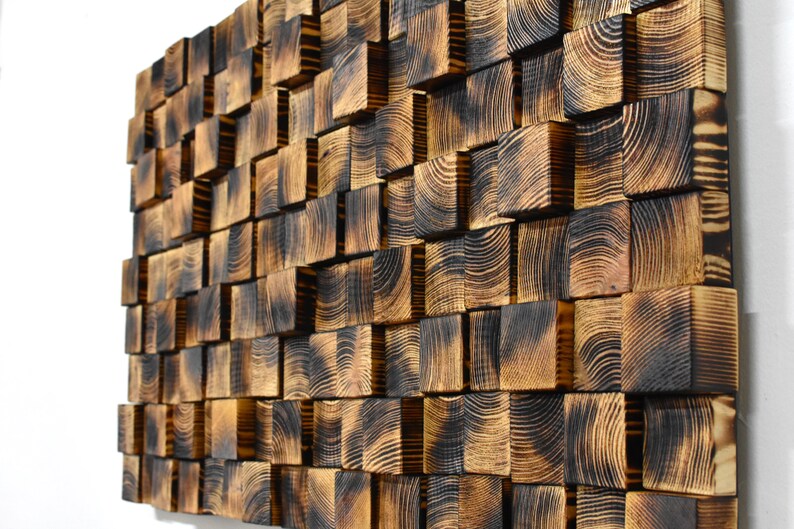 Puede incluir: Una pieza de arte de pared hecha de cuadrados de madera quemada, dispuestos en un patr&oacute;n escalonado. La madera tiene un color marr&oacute;n oscuro con patrones de veta visibles.