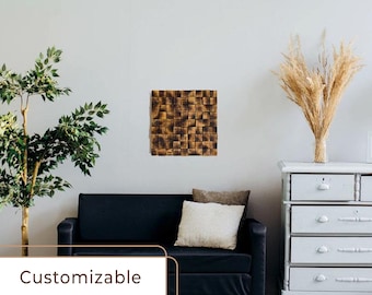 Puede incluir: Una pieza de arte de pared de madera marrón con un diseño geométrico, colgada en una pared blanca sobre un sofá negro. El arte de pared está hecho de cuadrados de madera individuales que están dispuestos en un patrón escalonado. El arte de pared está en un ambiente de sala de estar con una cómoda blanca y una planta en maceta.