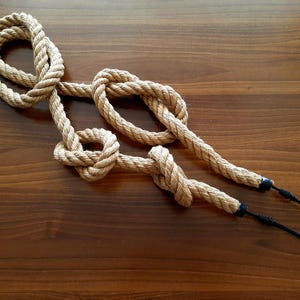 May include: A close-up of a brown rope with two black electrical cords attached to the ends. The rope is tied in a series of knots.