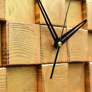 Puede incluir: Un reloj de madera en tono dorado con manecillas negras. La esfera del reloj est&aacute; hecha de bloques de madera apilados.