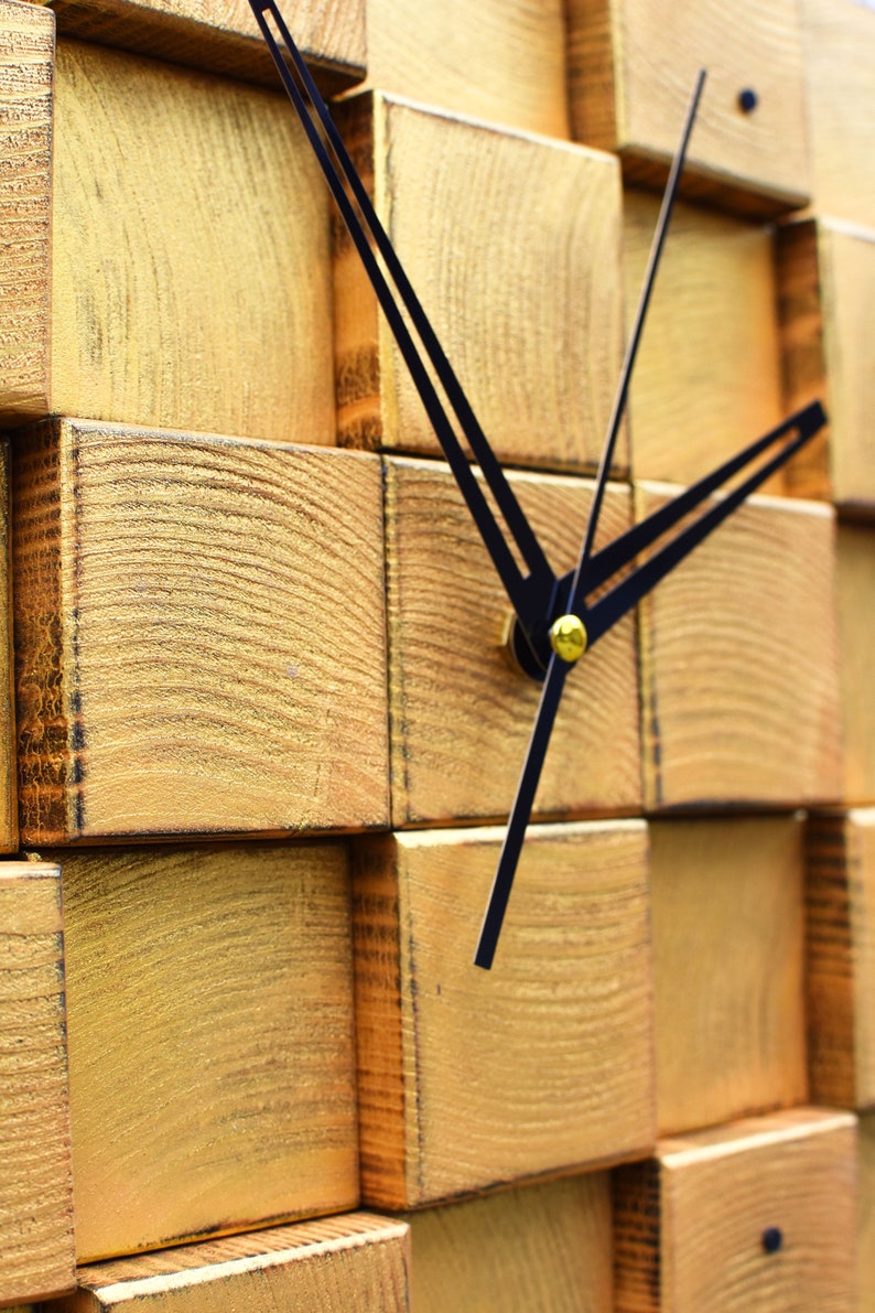 Puede incluir: Un reloj de madera en tono dorado con manecillas negras. La esfera del reloj est&aacute; hecha de bloques de madera apilados.