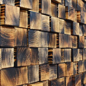 Puede incluir: Una pared hecha de bloques de madera quemada, dispuestos en un patr&oacute;n escalonado. La madera tiene un color marr&oacute;n oscuro con patrones de veta visibles.