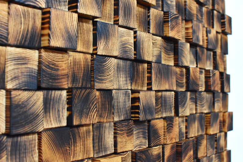 Puede incluir: Una pared hecha de bloques de madera quemada, dispuestos en un patr&oacute;n escalonado. La madera tiene un color marr&oacute;n oscuro con patrones de veta visibles.