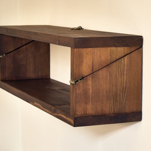 May include: A dark brown wooden shelf with a unique angled design. The shelf is mounted to a wall and has a simple, rustic look.
