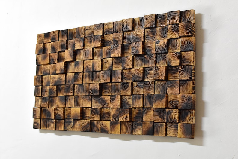 Puede incluir: Una pieza de arte de pared hecha de cuadrados de madera quemada, dispuestos en un patr&oacute;n aleatorio. La madera tiene un color marr&oacute;n oscuro con una superficie ligeramente texturizada.