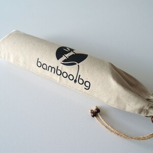 May include: A beige canvas bag with a drawstring closure and brown wooden toggles. The bag has a black logo that says "bamboo.bg" and a stylized image of a bamboo plant.