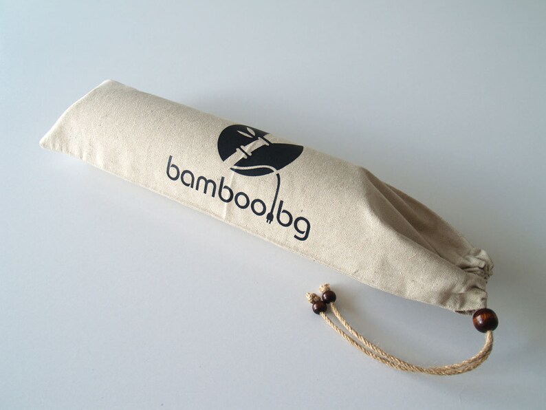 May include: A beige canvas bag with a drawstring closure and brown wooden toggles. The bag has a black logo that says "bamboo.bg" and a stylized image of a bamboo plant.