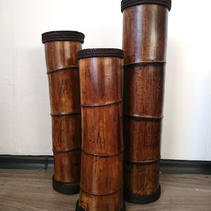 May include: Three brown bamboo cylinders with black rope trim. The cylinders are different sizes and are stacked on top of each other.